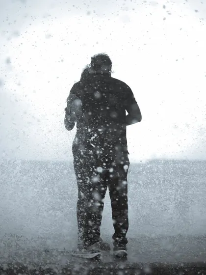 A black and white photo series capturing the spirit of Mumbai's monsoon at Marine Drive. People are seen enjoying the high tide, getting drenched by waves, and finding joy in the downpour.