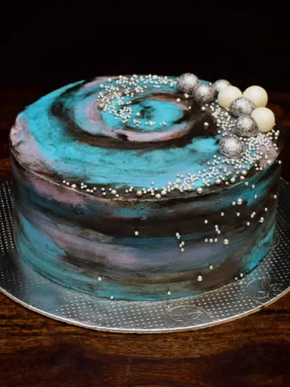 Another take on the galaxy theme, this time in shades of blue, purple, and black. The cake is decorated with silver sprinkles and chocolate spheres to look like planets and stars.