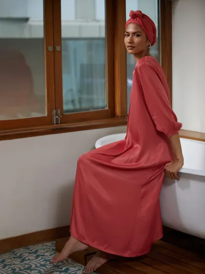 A full-length shot that showcases a beautiful, flowing abaya-style dress in a contemporary indoor setting. The pose is elegant and serene, highlighting the graceful drape of the fabric.