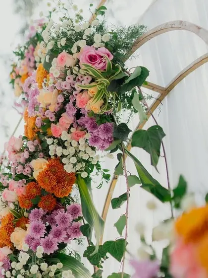 A detailed view of a colorful floral arrangement on a bamboo arch, showcasing a vibrant mix of marigolds, roses, and chrysanthemums.