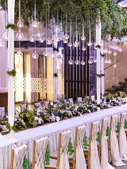 A long head table adorned with hanging glass baubles and a runner of fresh greenery. This unique and enchanting decor highlights our commitment to creating bespoke and unforgettable event designs.