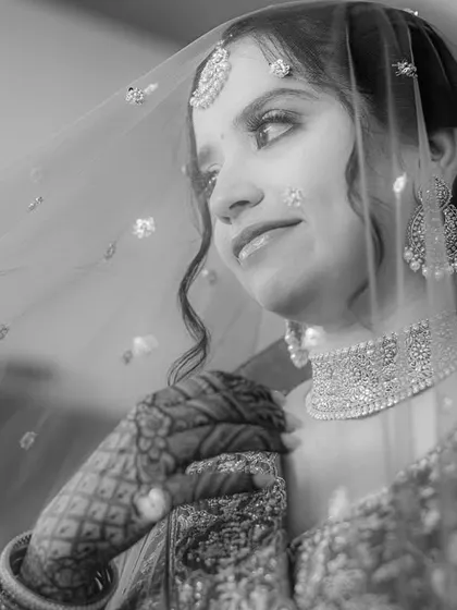 A thoughtful black and white portrait. The bride, holding her veil, looks away with a gentle smile, capturing the anticipation of the moments to come.