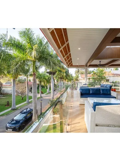 A view from the luxurious villa balcony, looking out onto the tree-lined street. The glass railing ensures an unobstructed view, making this outdoor oasis feel connected to the surrounding nature.