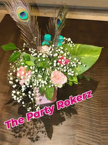 A top-down view of a small floral centerpiece with roses, baby's breath, and peacock feathers, perfect for adding a festive touch to tables.