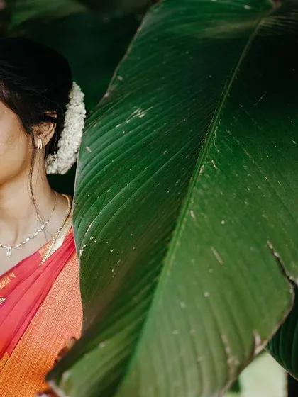 A serene portrait of a South Indian bride with her eyes closed, framed by a large green leaf.
