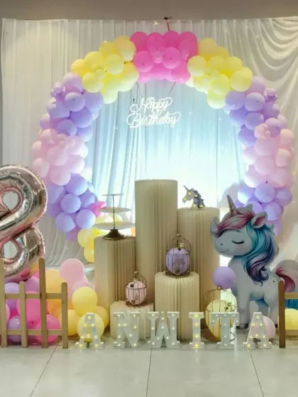 A dreamy unicorn themed eighth birthday party. The setup includes a pastel balloon arch, a large unicorn prop, and a picket fence for a magical touch.