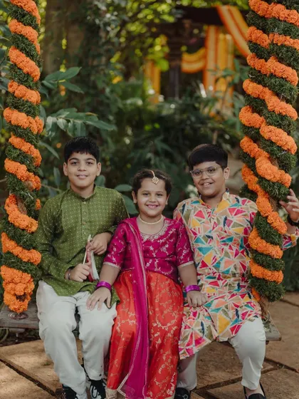 Three young guests in traditional wear pose happily on the floral swing.