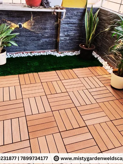 A close-up of a balcony makeover featuring WPC deck tiles, a strip of artificial grass, and potted plants. This combination of textures adds visual interest to the small space.