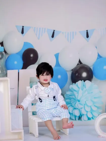 A dapper little gentleman celebrating his first birthday. He is sitting on a small white bench in a blue, white, and black themed setup.