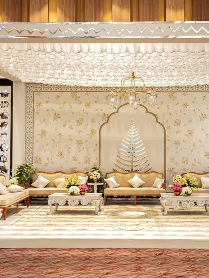 A full view of the white and gold lounge setup. The space is cohesive and luxurious, with a floral-patterned backdrop, intricately carved tables, and a beautiful ruffled fabric ceiling.