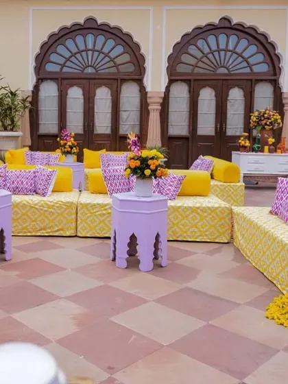 Another view of the royal-themed Haldi seating, showing the arrangement of low diwans and side tables against the backdrop of the palace architecture.