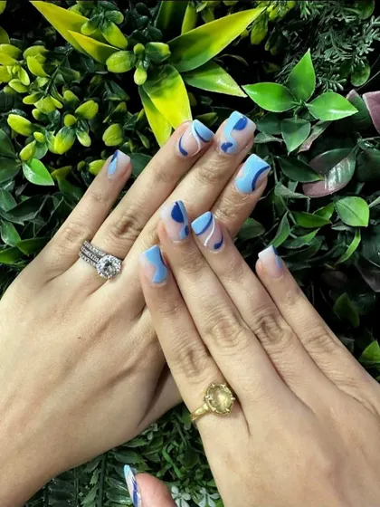 A cool and contemporary abstract design featuring organic shapes in shades of light and dark blue over a natural base. This manicure is a perfect example of modern, minimalist nail art.
