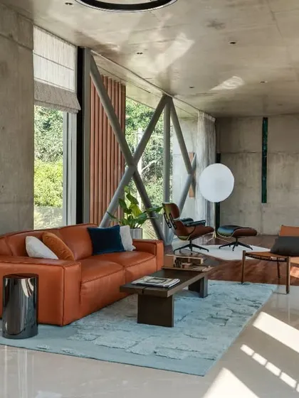 This living area in the Long House is defined by its raw concrete walls and exposed structure. A pop of color from the orange sofa adds warmth to the industrial aesthetic.