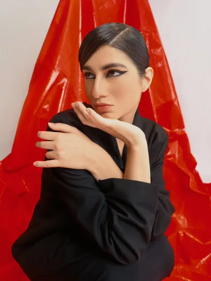 A chic and sophisticated portrait with a dramatic winged eyeliner. The contrast between the black outfit and the red background is striking.