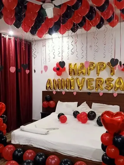 A classic red and black anniversary room setup with ceiling balloons and heart-shaped balloon pillars.