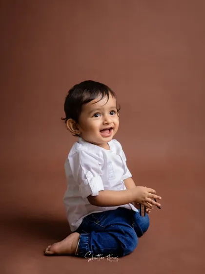 A candid moment of laughter from the same toddler, captured against a simple brown backdrop.
