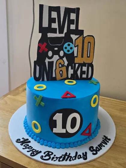 A blue gaming cake marks a tenth birthday, with a controller-themed topper and colourful game-button details around our cake.