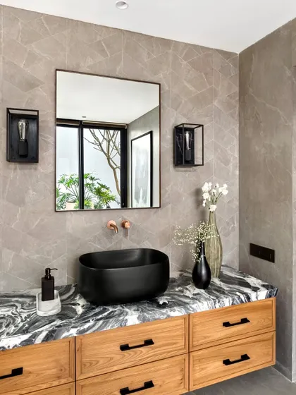 In the Mango Orchard House, this bathroom features a vanity with a striking black and white marble top. The black vessel sink and industrial-style sconces add a modern, graphic contrast.