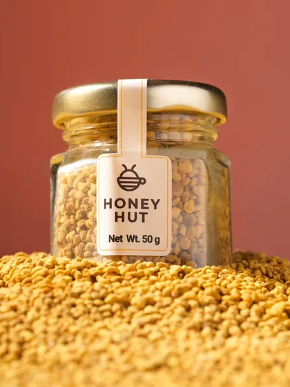 A close-up hero shot of a jar of bee pollen sitting on a mound of the product. This macro shot emphasizes the texture and natural quality of the ingredient.