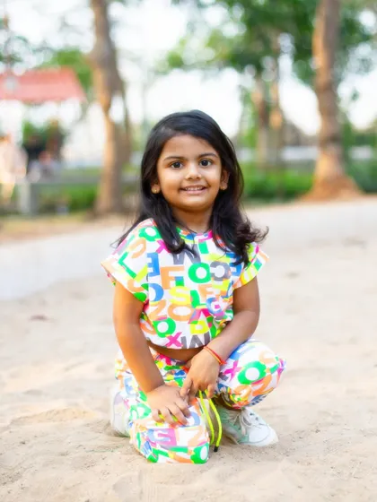 A bright, happy portrait in the sand. The colorful outfit and her direct, smiling gaze make this a vibrant and engaging photo that captures her playful nature.