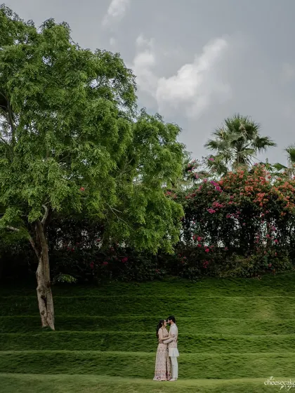 A wide-angle shot showing the couple surrounded by the vast, beautiful green landscape. It's about capturing love in nature.