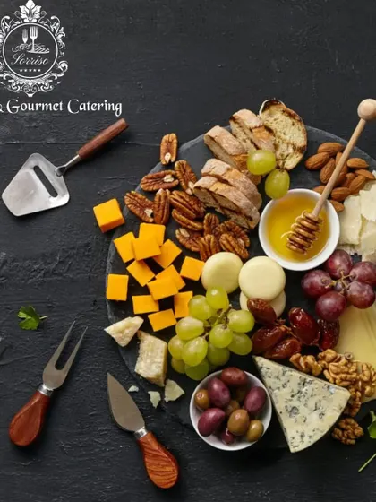 A stunning overhead view of a fully loaded charcuterie board on a dark slate platter. It features a diverse mix of cheeses, nuts, dates, olives, honey, and grilled bread, showcasing a complete tasting experience.