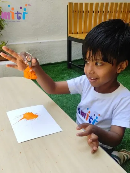 A young boy joyfully participates in our Holi celebration, using a pom-pom to dab bright orange paint onto paper. We celebrate the festival of colors with safe and creative art activities.