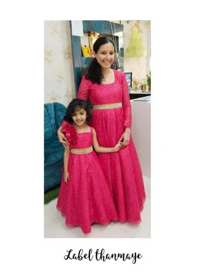 A bright and happy mother-daughter duo in matching pink gowns. The daughter's dress has a cute floral detail on the shoulder.
