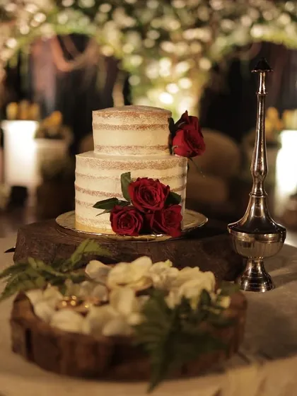 A beautiful two-tiered naked cake adorned with fresh red roses, sitting on a rustic wooden stand. This simple yet elegant presentation is perfect for a rustic or bohemian-themed wedding.