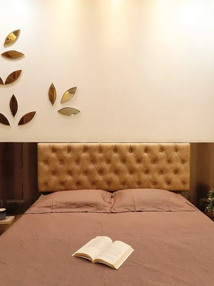 A simple and elegant bedroom setup with a tufted tan headboard and dark wood furniture. The wall is adorned with leaf-shaped mirror accents, adding a decorative touch without overwhelming the space.