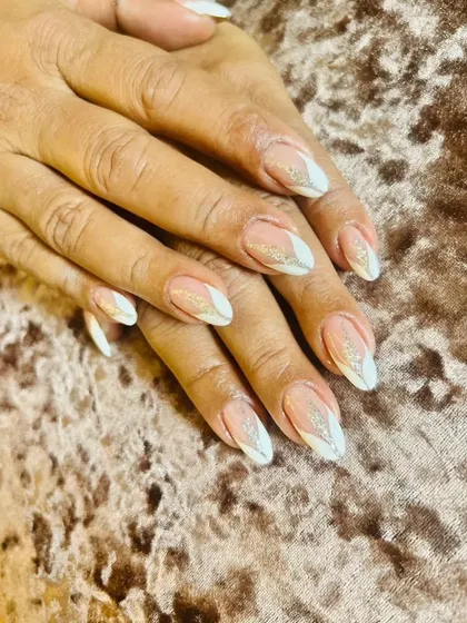 An elegant, pointed almond nail set with a petal-like white tip design and a dusting of fine gold glitter.