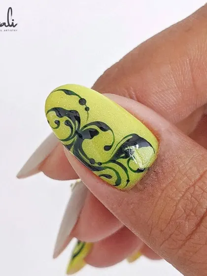 A close-up of the neon yellow and black swirl art on a client's nail. The detail is everything.