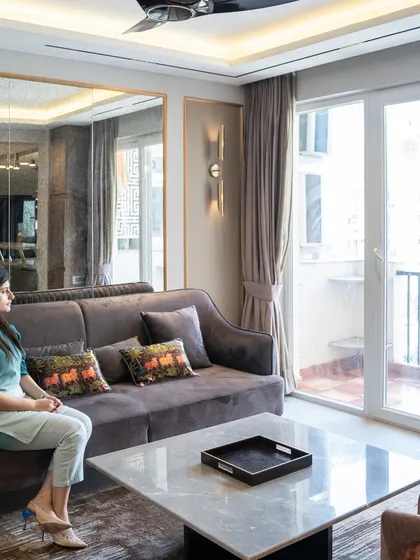 Our founder, Amrita Maitra, enjoying a moment in a recently completed apartment. The space features a comfortable sofa, a marble-topped coffee table, and large glass doors that open to a balcony, filling the room with natural light.