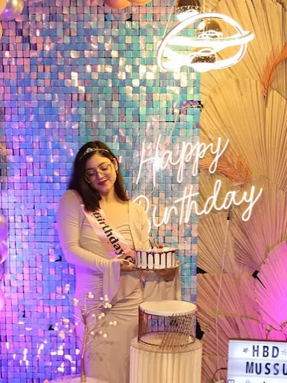 A smiling birthday girl holds her cake in front of a "Happy Birthday" neon sign. Our setups are designed to make the guest of honor feel truly special.