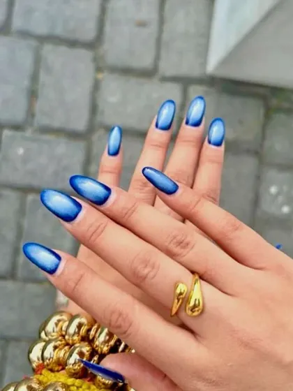 A vibrant blue aura or cat eye effect on long almond nails. The deep blue edges fade into a bright, glowing center for a mesmerizing look.