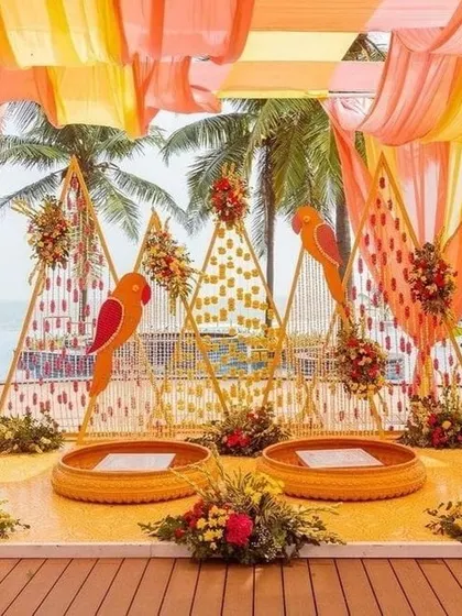 For a beachside mehendi, I designed this vibrant setup with parrot motifs and triangular backdrops. The decor uses a warm color palette of orange and yellow drapes, reflecting the fun and festive mood of a destination wedding.