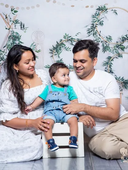 A relaxed and happy family portrait in a bohemian-themed studio setting. The parents look lovingly at their child, creating a warm and natural family photo.