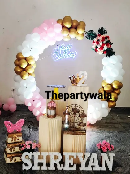 A pink, white, and gold balloon ring with a 'Happy Birthday' neon sign.