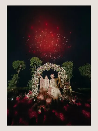 A moment of pure spectacle. This shot captures the couple under a floral arch as fireworks light up the night sky, a grand and unforgettable finale to their wedding celebration.