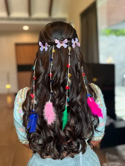 A minimalist and colorful hairstyle for a haldi ceremony. The soft curls are adorned with feathers and butterfly clips for a fun, bohemian vibe.