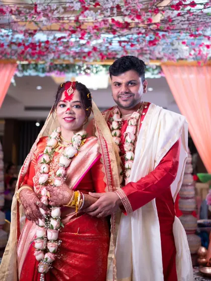 A classic portrait of a newly married Bengali couple under the floral mandap after the completion of their wedding rituals.