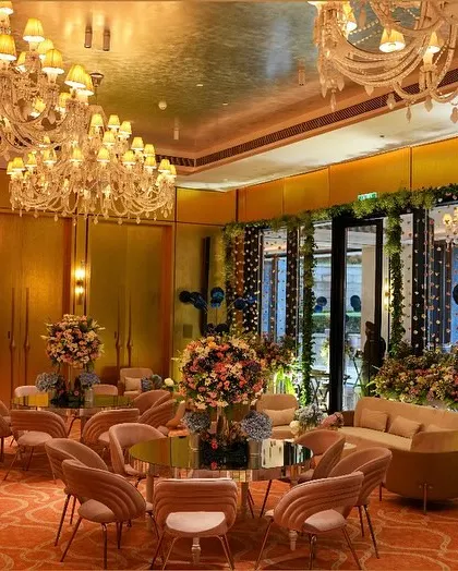 A wider view of the pastel-themed event space, showing the elegant seating arrangements and grand chandeliers inside a sunlit room.