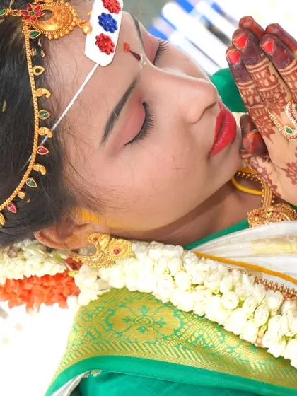 A candid moment of a bride in prayer during a wedding ritual, her hands covered in intricate mehndi.