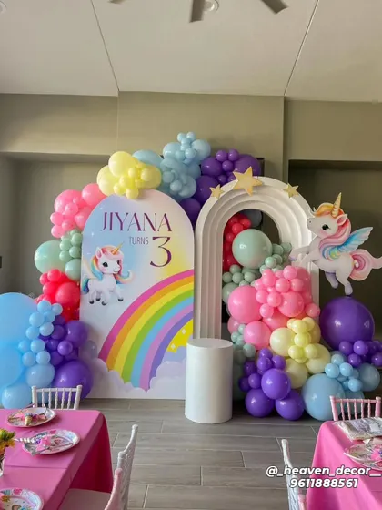 A colorful rainbow unicorn theme for a third birthday. This decor features a double-arched backdrop, a cascade of rainbow-colored balloons, and cute unicorn cutouts.