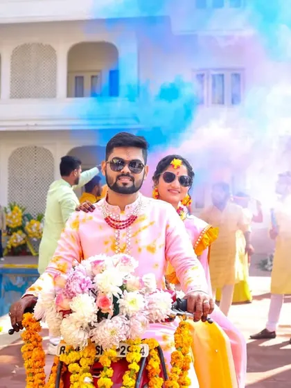 A fun-filled Haldi moment by the pool. The couple on a flower-adorned bicycle surrounded by blue smoke creates a unique and memorable image.