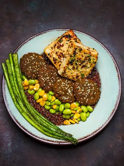 A gourmet falafel and quinoa bowl with edamame, asparagus, and grilled halloumi, styled with a dark, moody aesthetic.
