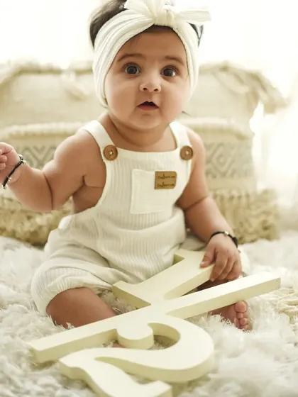 A slightly different angle from the six-month session, capturing a curious and sweet expression. The simple white outfit and background keep the portrait feeling fresh and timeless.