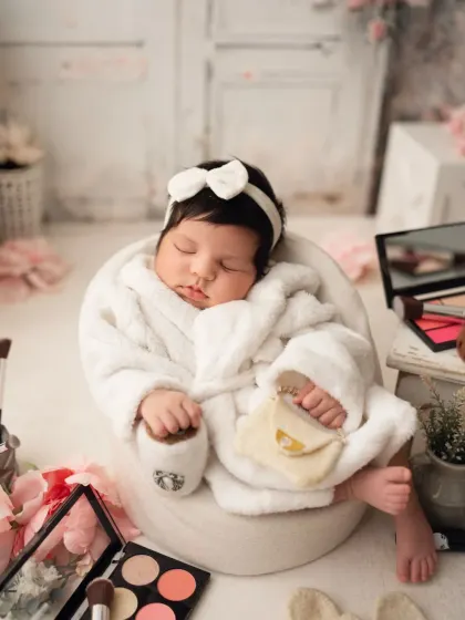 A spa day for the newest diva. This newborn is enjoying a "relaxing" day in her bathrobe, surrounded by makeup brushes and palettes.
