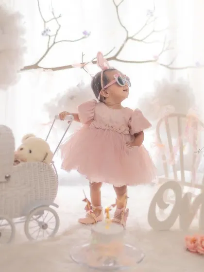 A full view of the stylish first birthday setup, complete with a wicker pram, teddy bear, and the number "One". Every detail is curated to create a perfect scene.