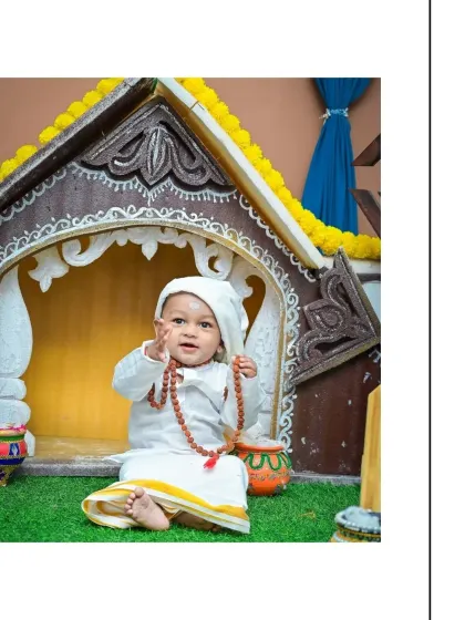 This little one, dressed as Sai Baba, smiles sweetly while playing with his prayer beads. The warm, inviting set makes for a comfortable and peaceful photoshoot experience.